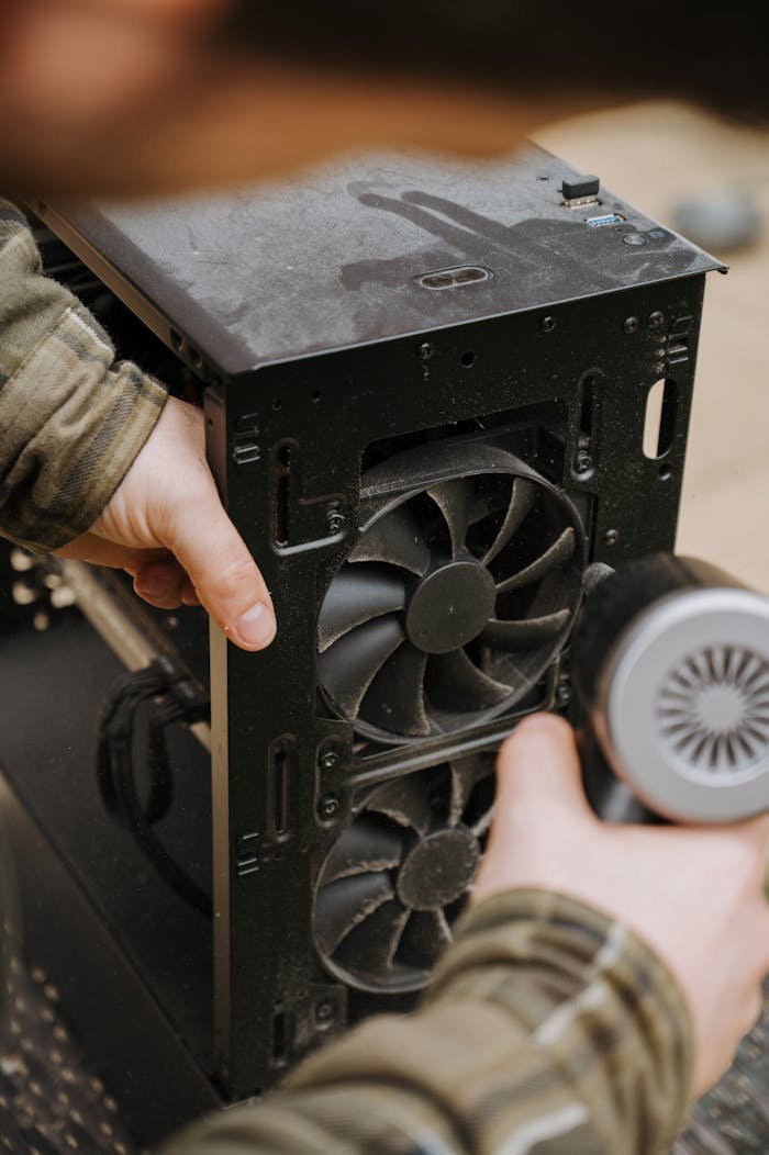 about-04 Hands cleaning dust from a computer fan using an electric air duster for maintenance.
