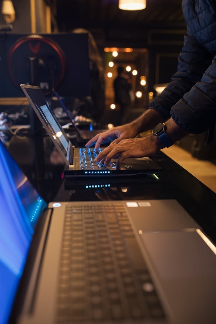 services-06 An individual typing on a laptop in a dimly lit modern workspace, emphasizing technology and focus.